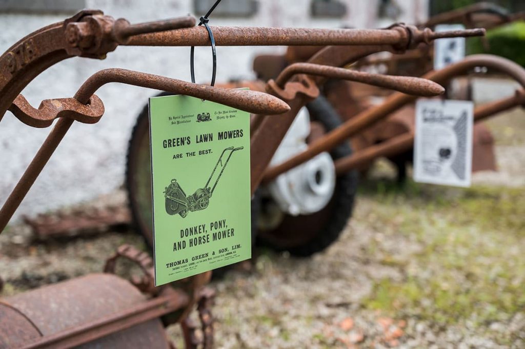 An old, rusty lawnmower with faded paint and worn metal parts.
