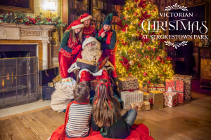 Santa with his three elves in the library of Strokestown Park House with two children sitting in front of him.
