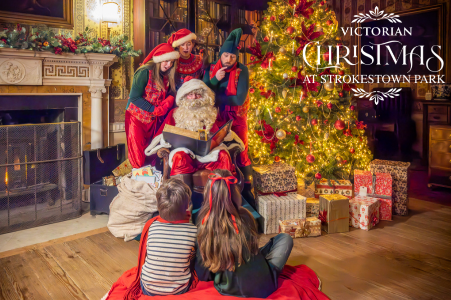 Santa with his three elves in the library of Strokestown Park House with two children sitting in front of him.