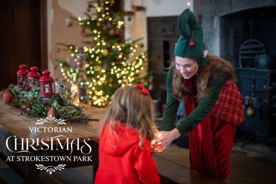 Elf handing a gift to a little girl in a red coat as part of the Victorian Christmas Experience, Strokestown Park.