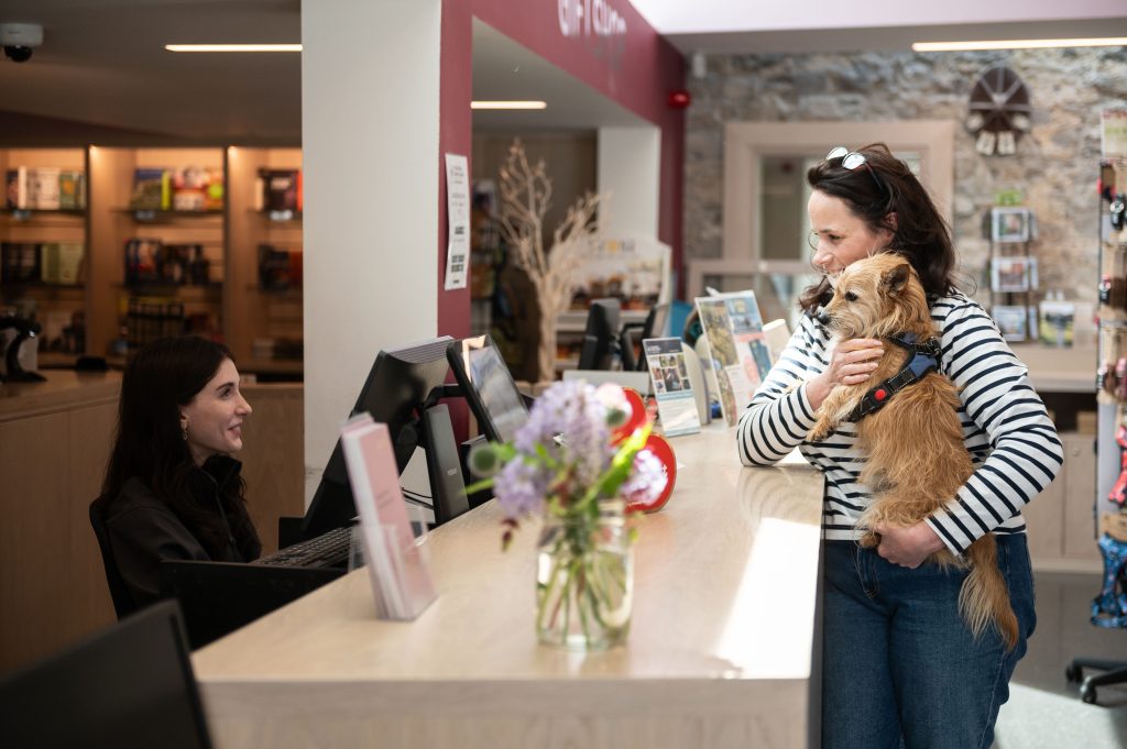 A woman carrying a small dog standing at the welcome desk at the visitor centre at Strokestown Park